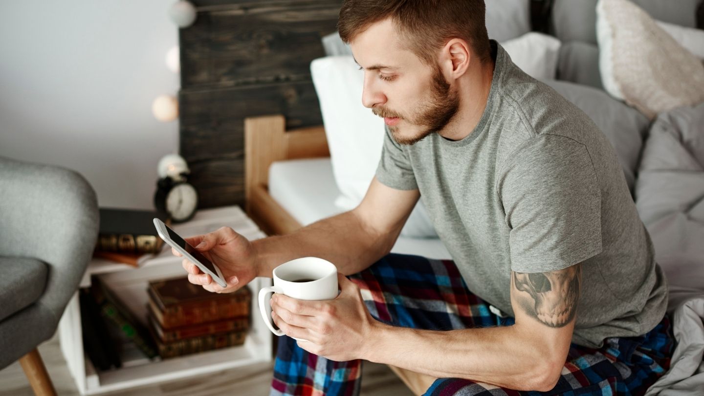 man holding coffee mug and smartphone looking at text