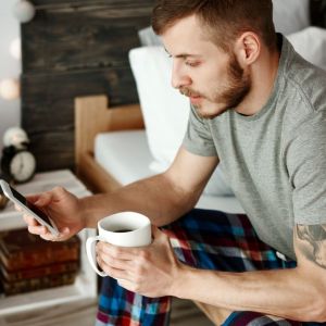 man holding coffee mug and smartphone looking at text