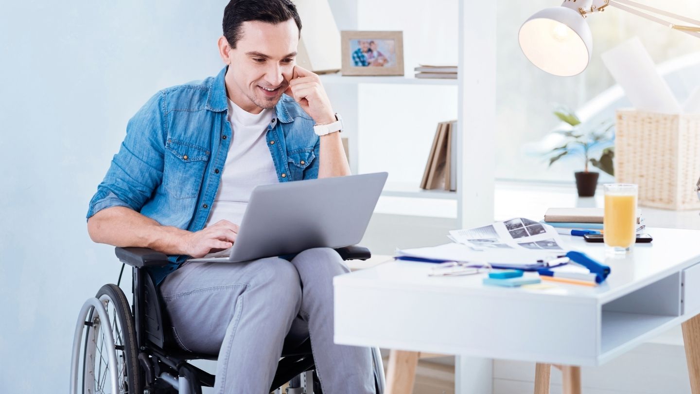 main in wheelchair using a laptop at a desk